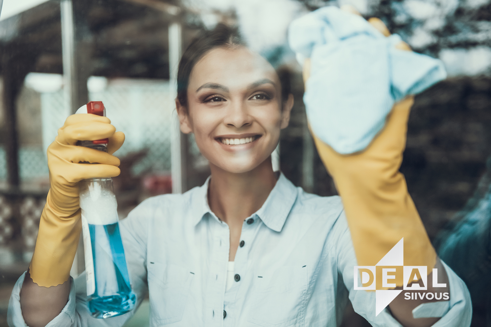 Hymyilevä siivooja pyyhkimässä ikkunaa mikrokuituliinalla, kädessä sininen puhdistussuihke ja keltaiset suojakäsineet, Deal Siivous -logo kuvassa.